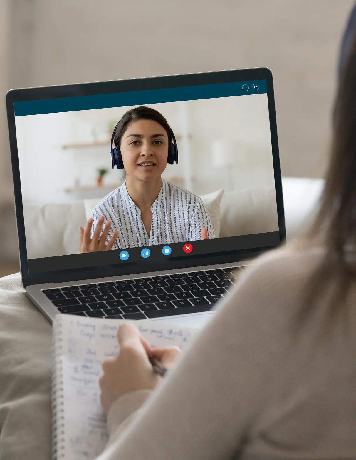 A woman video chatting on a laptop while taking notes.